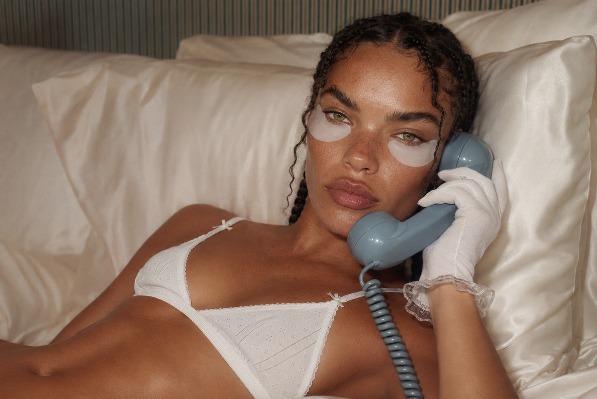 Woman wearing under-eye patches taking a call on a vintage rotary phone in bed