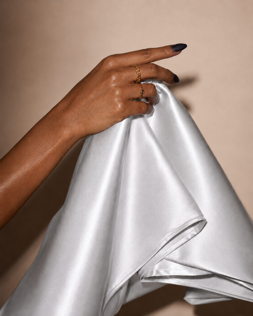 A hand feeling the weight of 22 momme Heirloom Silver copper-infused mulberry silk